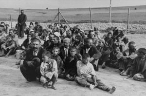 Romani prisoners sitting on the ground in a camp.