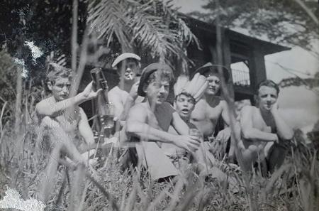 Six soldiers sitting in the tropical forest in Burma during World War 2. All are wearing army trousers or shorts without tops. Three are wearing hats. 