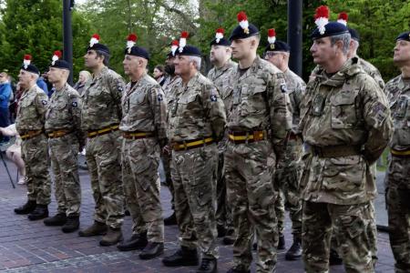 Two rows of Fusiliers standing at ease with their arms behind their backs. They are dressed in combat fatigues and caps with the distinctive red and white hackle. There are six soldiers in each row.