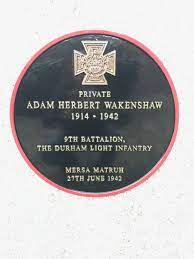 Black circular plaque with a a gold Victoria Cross at the top. The inscription reads Private Adam Herbert Wakenshaw, 1914 to 1942, 9th Battalion, Durham Light Infantry, Mersa Matruh, 20th June 1942