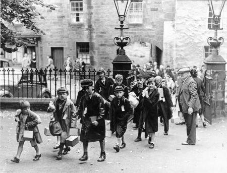 Group of childrenwho ae being evacuated leave school ready for their journey. They are carrying bags and suitcases. 