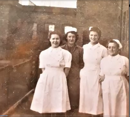 Four women standing in front of an old hospital building. Three are dressed in white nurses uniforms. The woman second from the left is dressed in a darker uniform an is possibly a porter. Norah is at the right end of the row. She is the smallest of the women at around 5 feet tall.