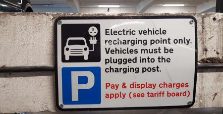 Electric charging sign, the sign has a picture of a car charging and states’ Electric vehicle recharging point only. Vehicle must be plugged into the charging post. Pay & Display charges apply (see tariff board)