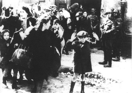 A young boy and a woman, possibly his mother, with their arms held up during the Warsaw Ghetto Rising while surrounded by armed German troops