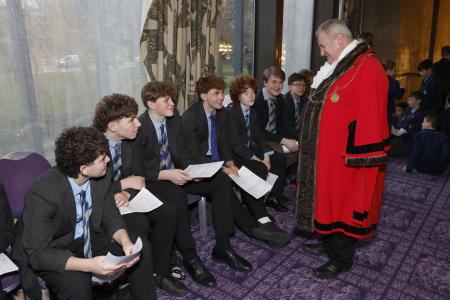 Seven male students from a school in Newcastle talking to the Lord Mayor of Newcastle, Councillor Henry Gallagher. The boys are wearing dark grey blazers, black trousers, pale blue shirts and blue stripy school ties. The Lord Mayor is wearing is red robes and chains