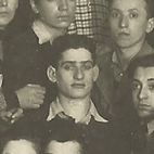 David Berger, aged about 20, with a group of young people in 1940. He has short dark hair and is wearing a dark jumper with a shirt underneath. Behind him are a woman and man of a similar age.
