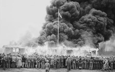 Image shows Belsen-Bergen concentration camp when allied troops liberated it. People who have been held captive are to the front of the photo watching as some of the huts are burned to clear the camp of disease.