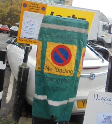 Ticket machine in car park covered with green hood, the hood has the no waiting symbol and states ‘no loading Parking place suspended’, also large yellow sign giving details of suspension