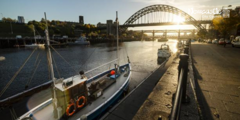 A boat is moored on the River Tyne, looking up at the Tyne Bridge on a sunny day