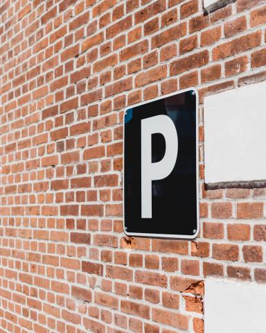 Photo showing a brick wall with a square parking sign with a white letter P on a dark background .
