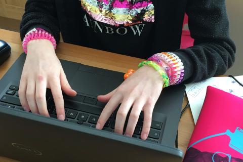 Image shows a child's hands typing on a laptop computer keyboard