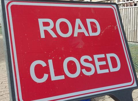 Photo showing a road sign with a red background the the words Road Closed in white letters