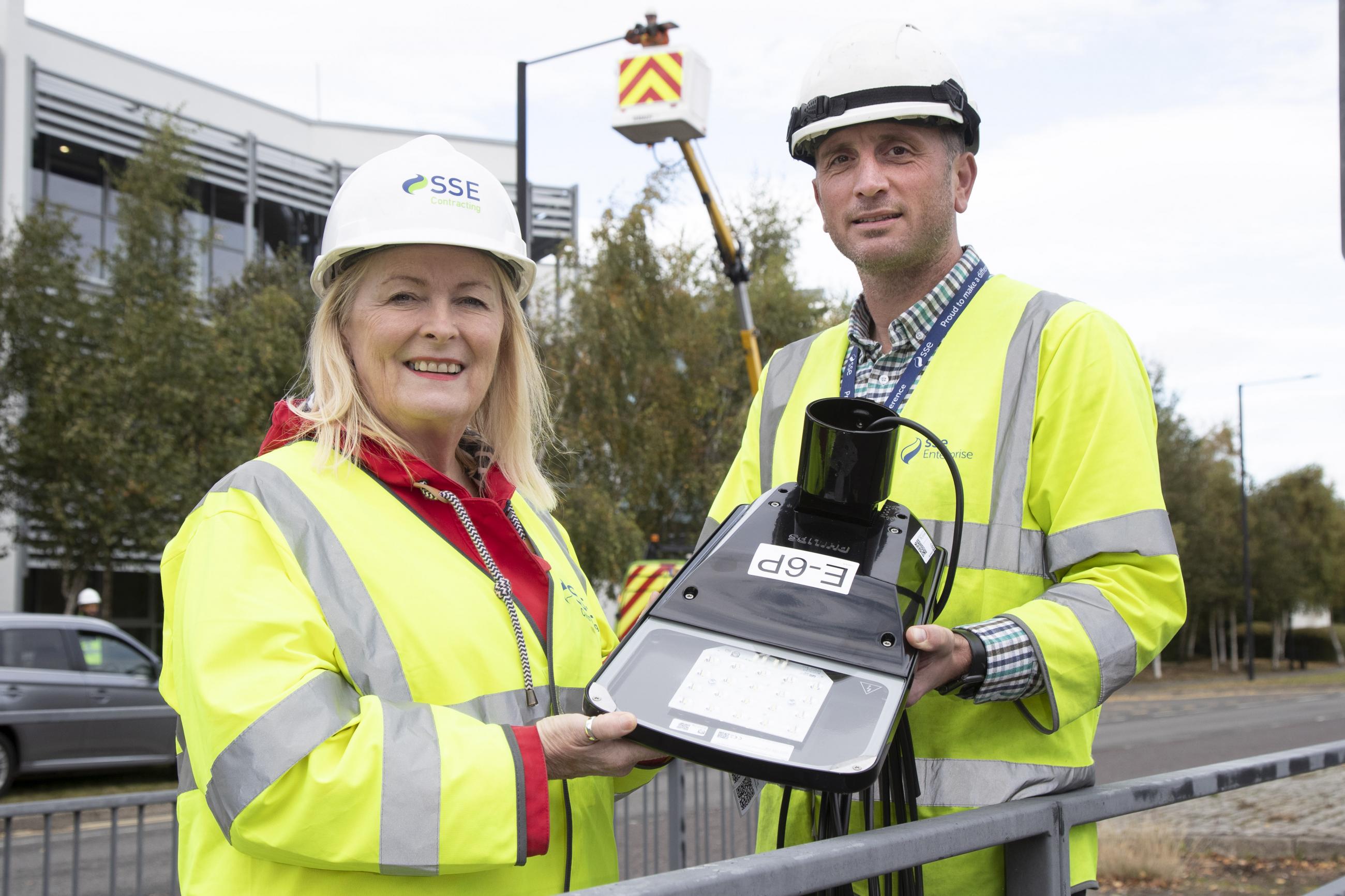 Photograph showing two people in hard hats and high vis jackets holding the lamp for a new street light.