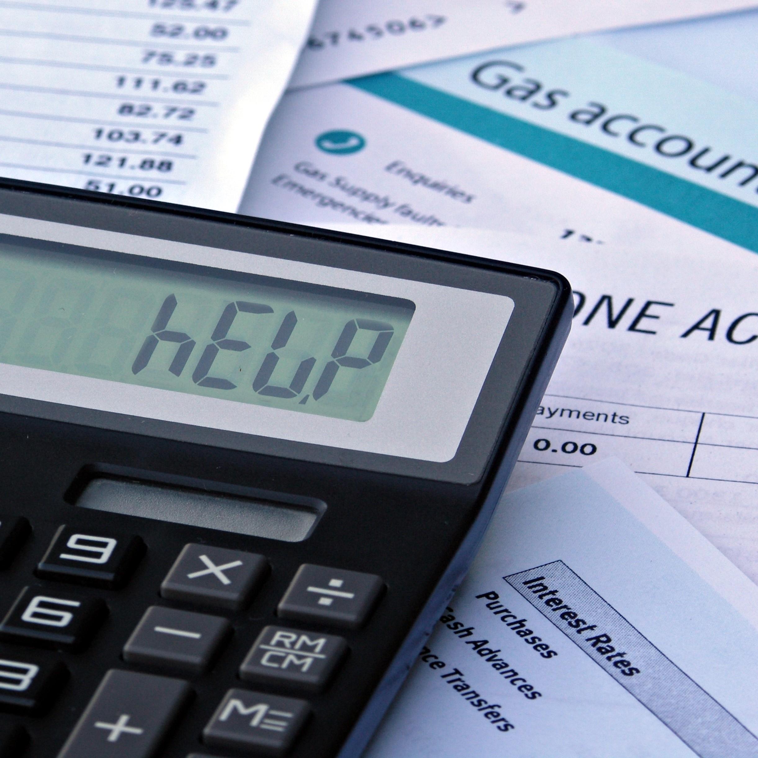 Photograph showing a calculator with the word 'help' displayed on the screen and surrounded by household bills.