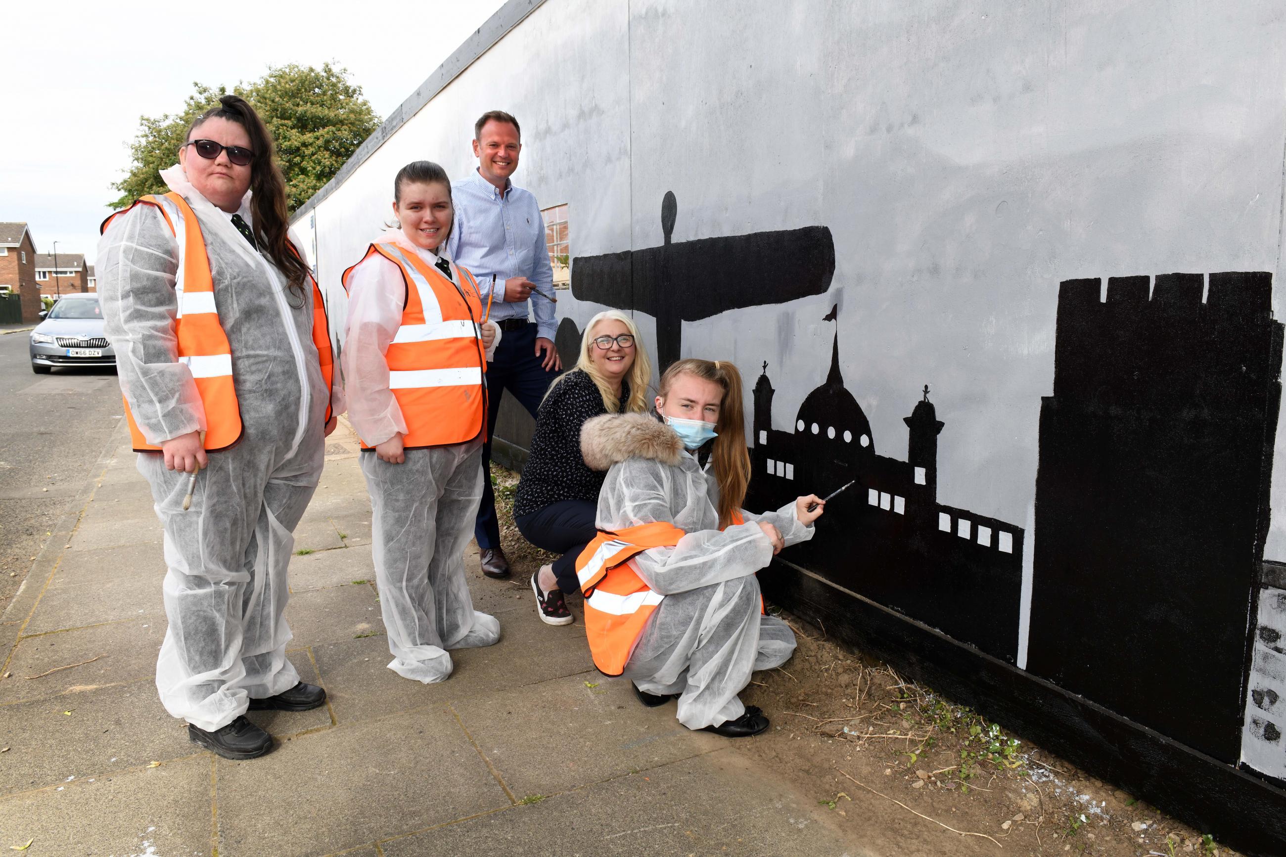 Pupils from Sir Charles Parsons School painting the mural. Pictured from left to right are Jessica Frame, Denise Newton, David Langhorne Asset and Development Director at Your Homes Newcastle, Linda Hobson Cabinet Member for Housing at Newcastle City Council and Demi-Leigh Oliver