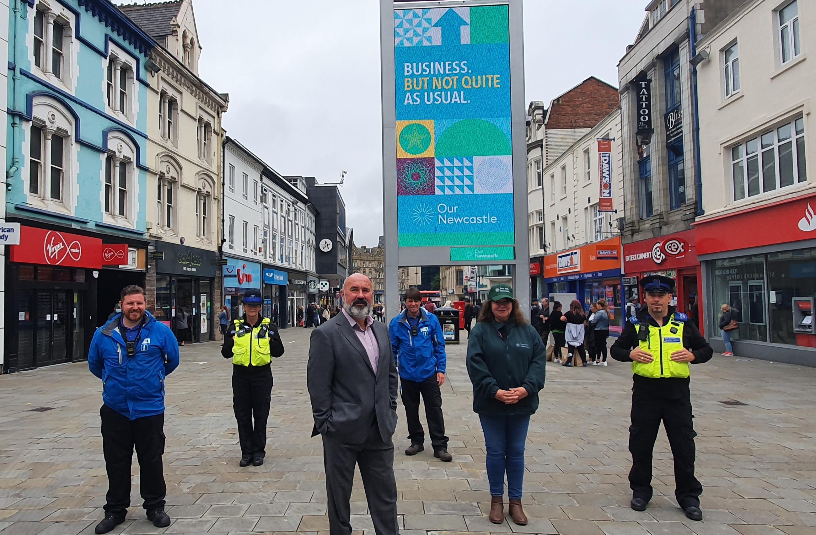 Six people stood, spaced apart on a shopping street.