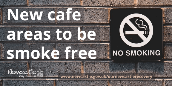 A black and white no smoking sign on a grey brick wall with the text New cafe areas to be smoke free