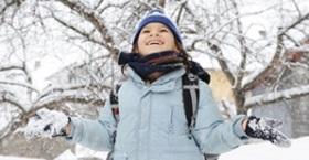 A girl in a blue coat and hat, with arms outstretched, in a snowy landscape